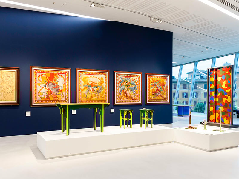Green and yellow chairs/stools displayed in front of a blue wall with red and orange artwork