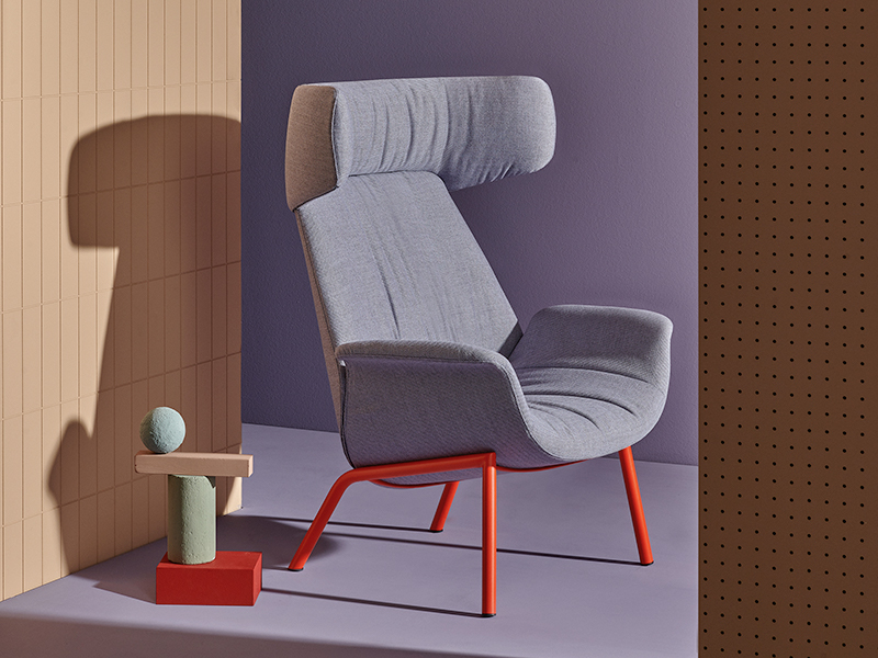Purple Ila chair with headrest and red metal legs in front of purple and peach walls, next to a side table