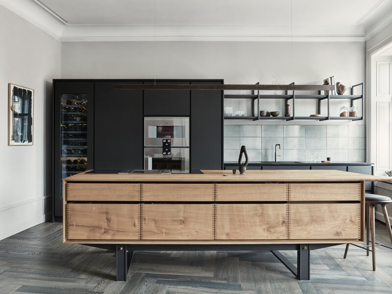 Bespoke Kitchens Oak wood kitchen island on grey wood flooring in front of black cupboards