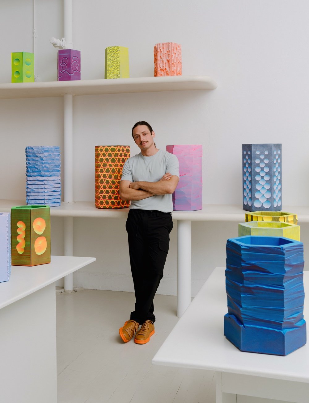 A portrait of Jamie Wolfond in front of the colourful sculptural vases his studio designed for Flash Set.