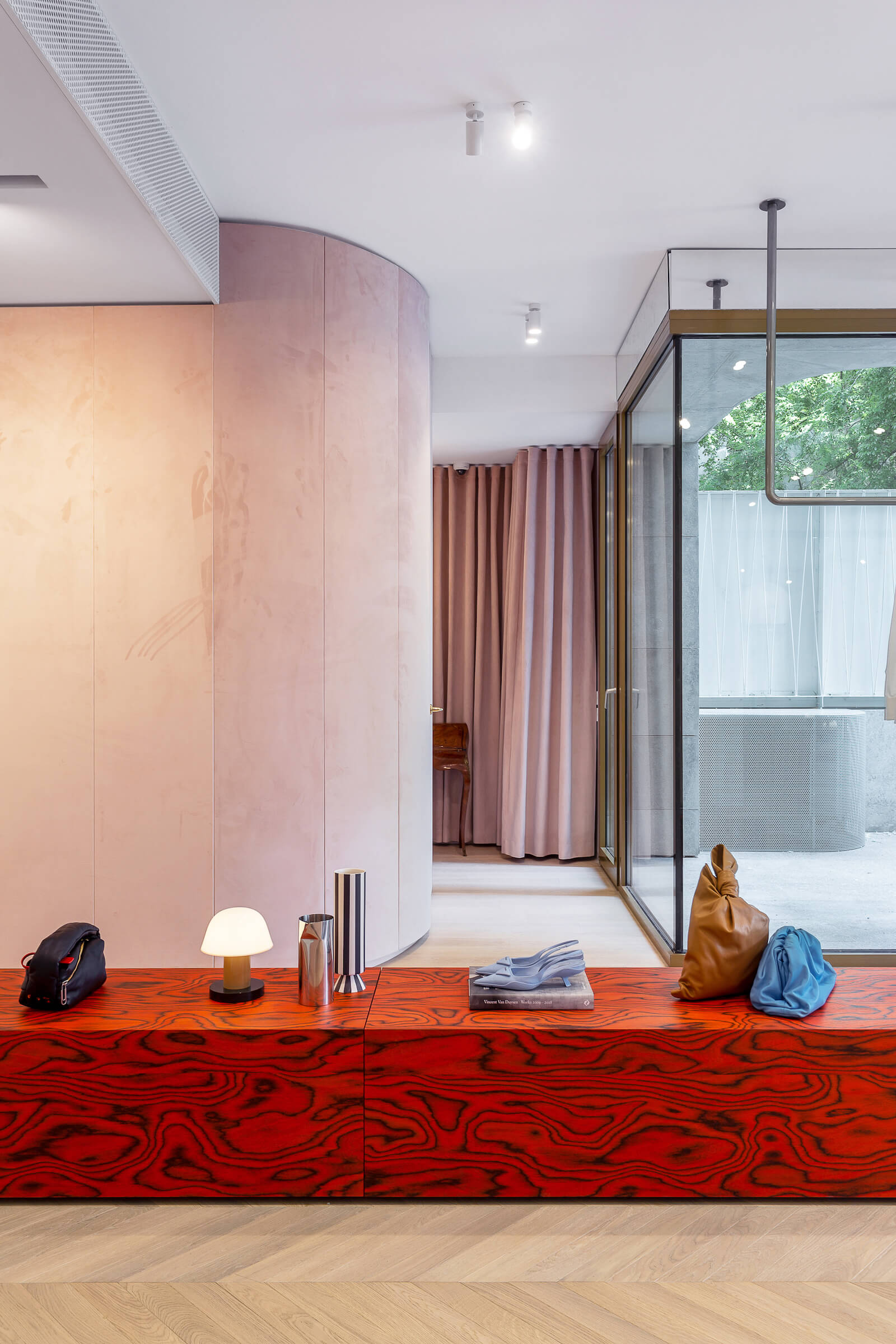 Pink velvet walls and curtains offset by ALPI Sottsass Orange veneer on merchandise platform at Aparterre clothing boutique in Bucharest, architect Bogdan Ciocodeica