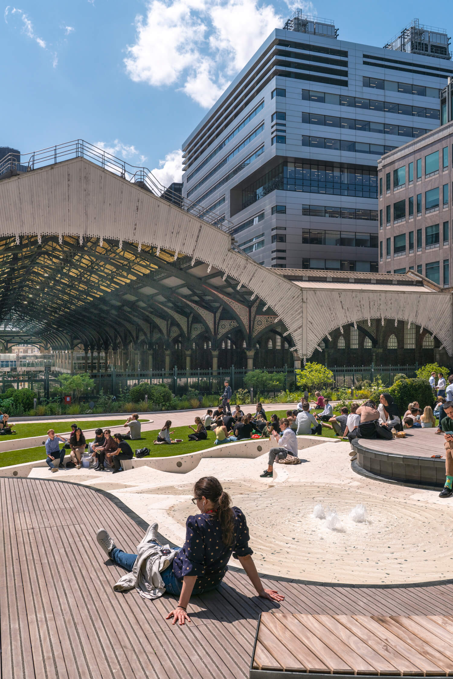 A woman sitting on the timber boardwark overlooking the social zones at the centre of London's Exchange Square.