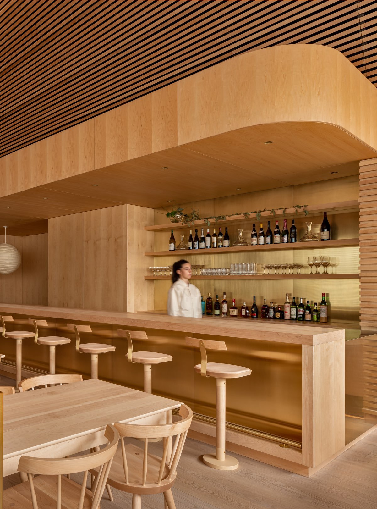 Wood barstools face a brass-backed bar in an otherwise all-wood space