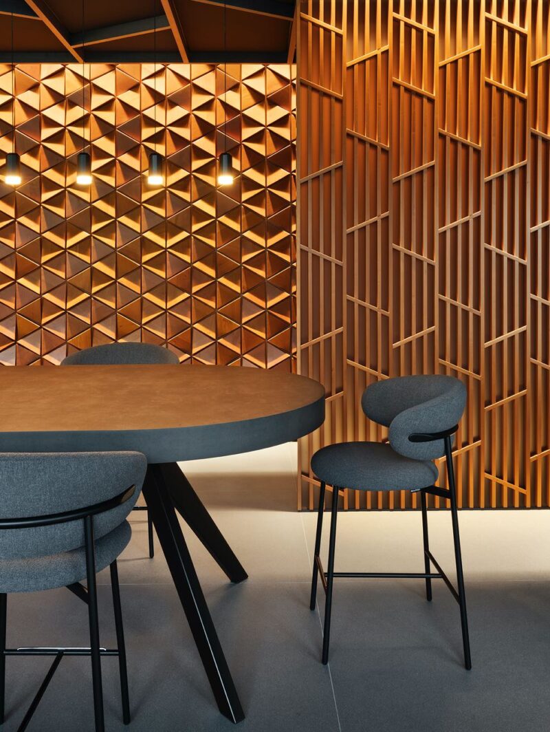 A dining table sits in front of a slatted partition that forms a hallway in front of a feature wall clad in small triangular wooden panels.