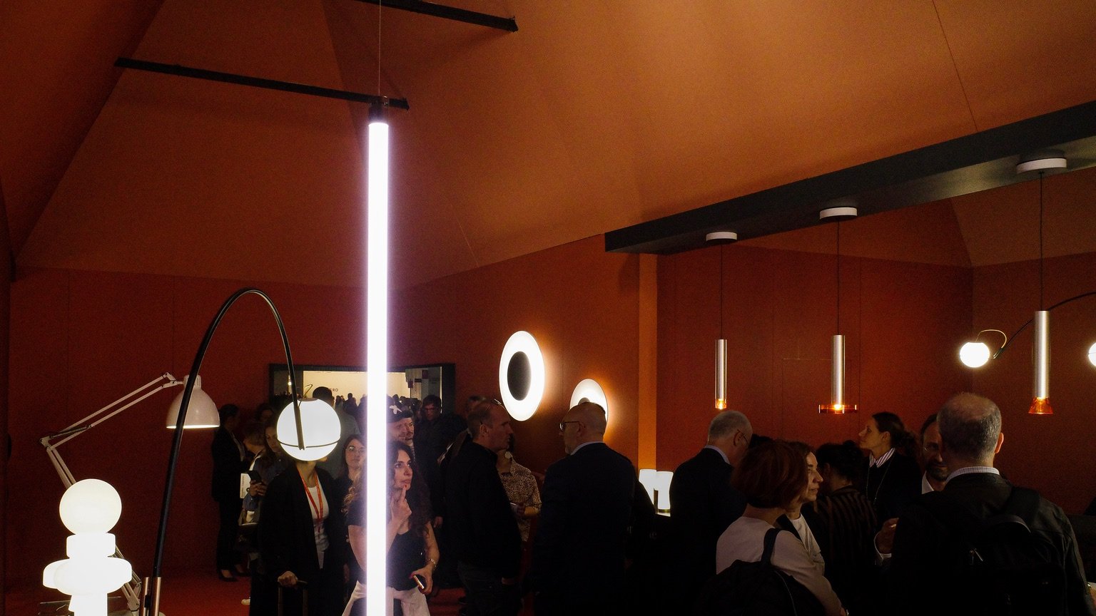 People inside of an orange house-shaped exhibition display at Euroluce 2023 featuring new lights from Fontana Arte.