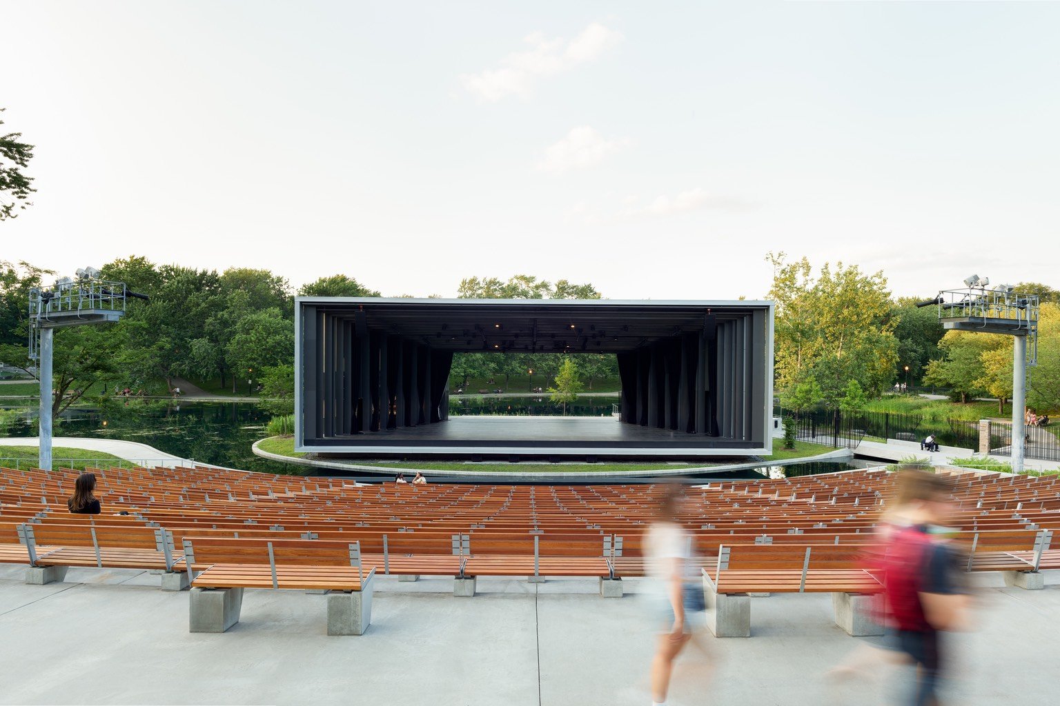 A person walks past the amphitheatre wood seating in front of La Fontaine Park's boxy Theatre de Verdure pavilion designed by Lemay.