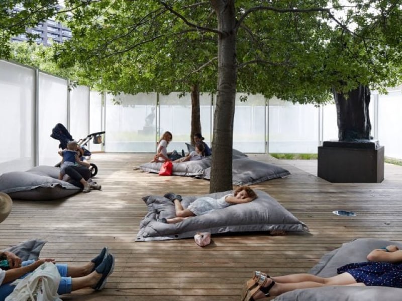 A group of people relaxing on cushions on a wooden surface underneath a tree.