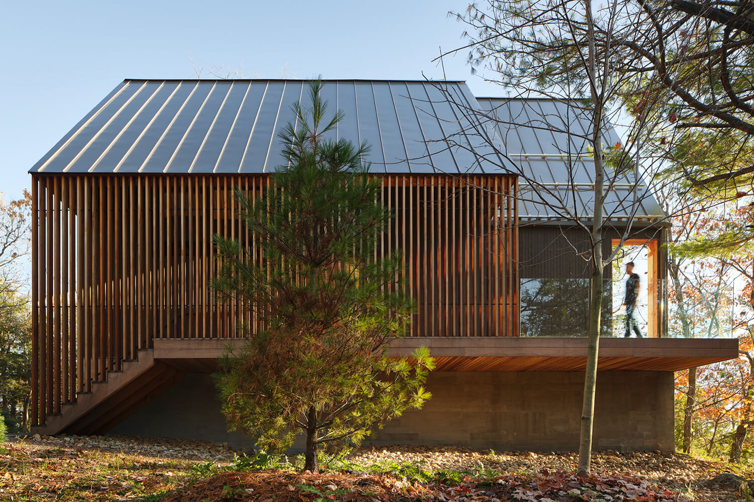 A cantilevered, wood-slat walkway leads to the main entrance and to the back porch, offering a “sense of procession from the landscape to the interior.”