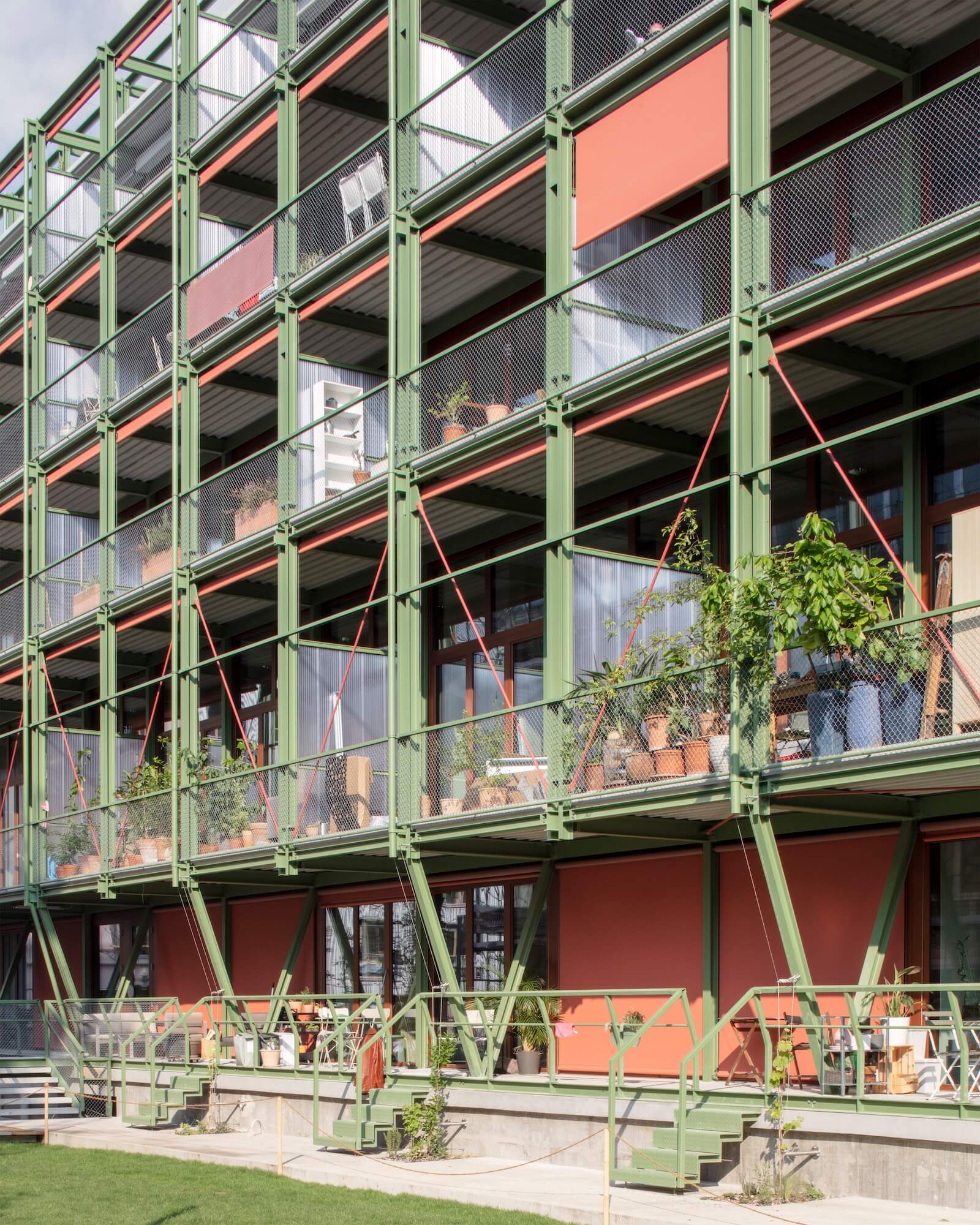 The southeast-facing façade of the new affordable apartment building in Basel, which was adapted from the Coop wine storage facility, expresses an eclectic character, with operable shades in terracotta and a light green metal frame system and railings.