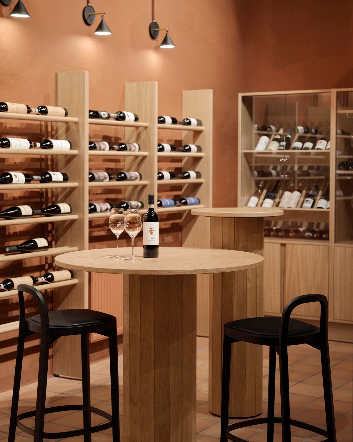 Counter height wood table with black stools in front of wine bottle storage