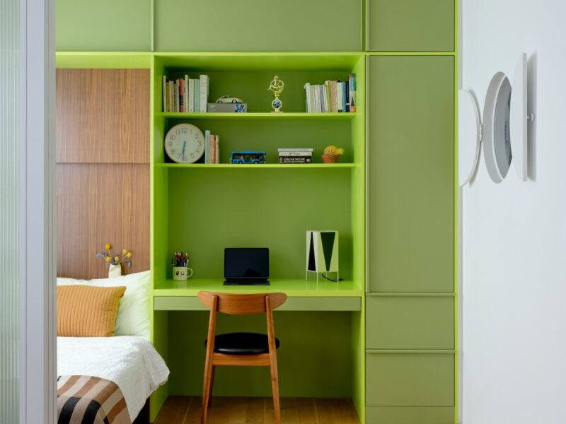 Lime green millwork creates shelving, a desk and a bed against the back wall of an NYC apartment reno by Ideas of Order Studio.