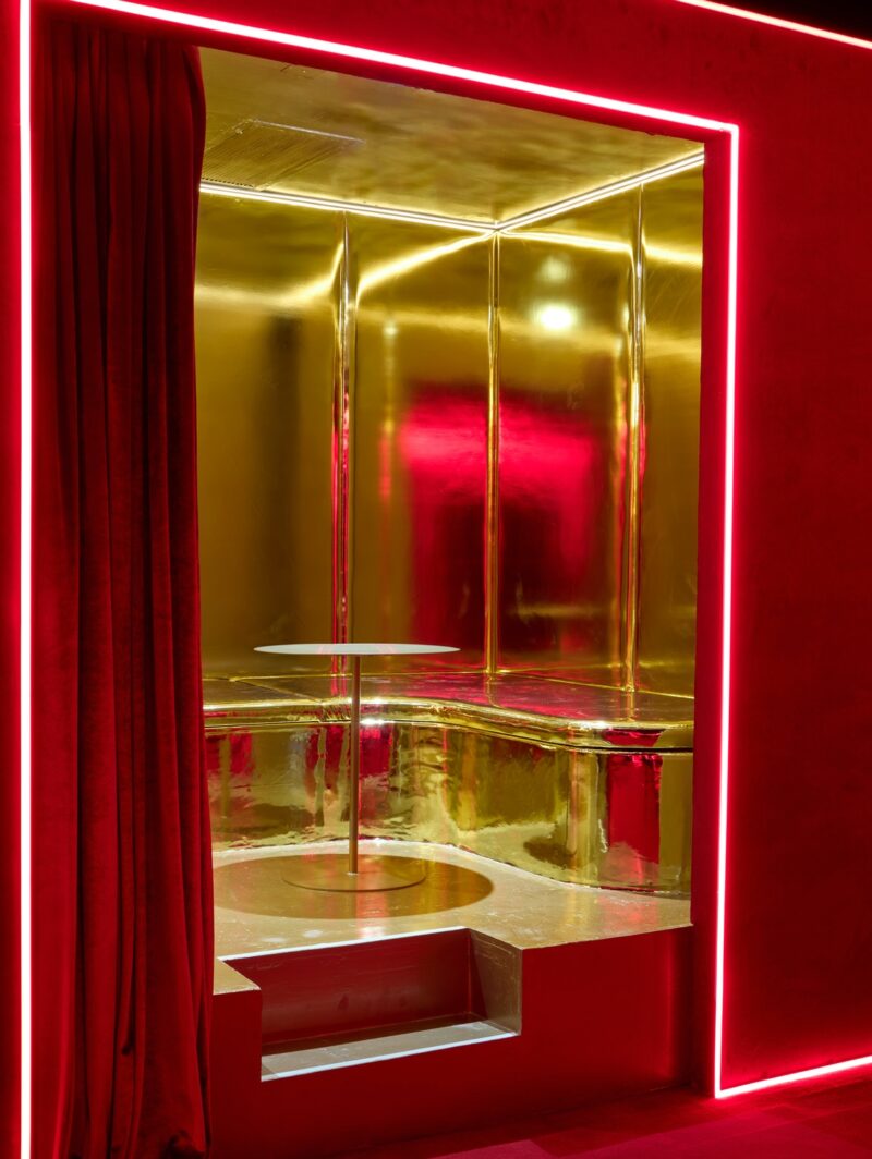 A closeup of one of the gold private rooms in Silencio NYC (a club designed by Crosby Studios and inspired by David Lynch), showing the built-in bench and central circular cocktail table. The room is two steps up from the main dance floor.