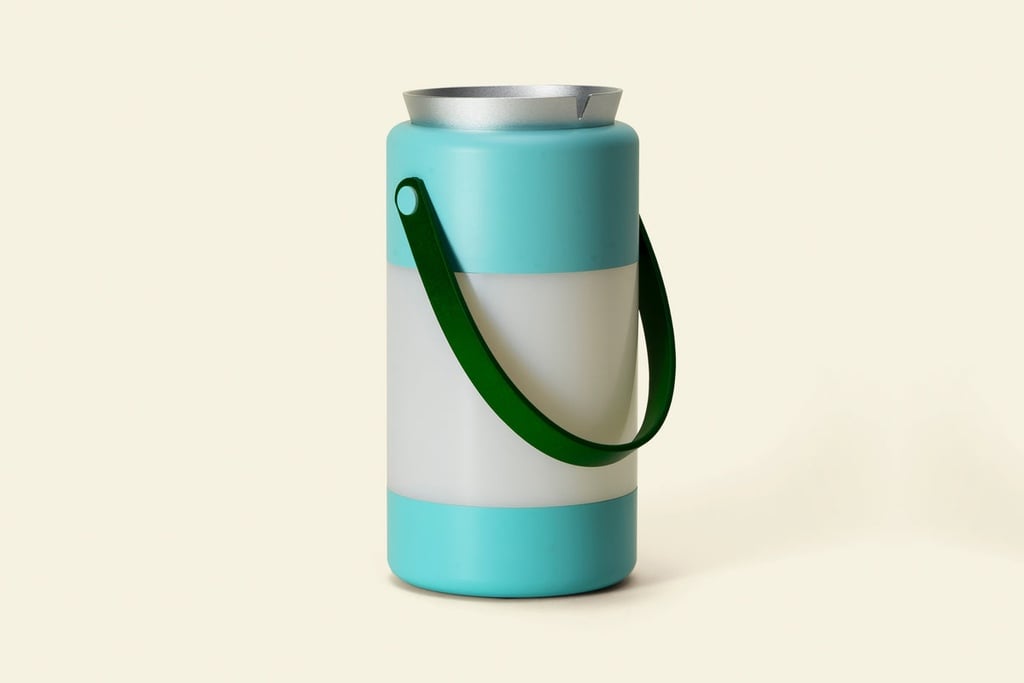 A lantern that looks like a retro thermos, with a green handle and aqua stripes on the top and bottom above a middle section that glows. The top features an aluminum ash tray. It's one of the products from Houseplant, a homeware line led by Seth Rogen. The designer behind it is the Toronto design studio Castor.