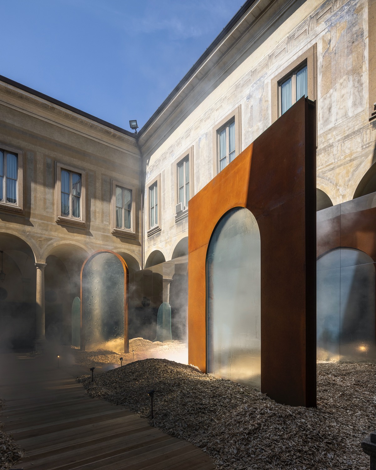 For Milan Design Week 2024, Lasvit presented a series of glass doorways framed in corten steel in a courtyard of a historic palazzo. Three of the screens are shown here at an angle.