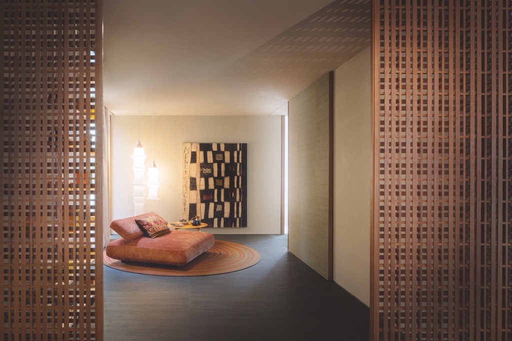 An orangey brown sofa sits in a living room area in front of a black and white abstract artwork and a hanging paper lantern. Slatted wooden screen doors are pulled open at the entrance to the room. Part of a Milan design week 2024 review that speaks to the value of quiet domestic spaces.