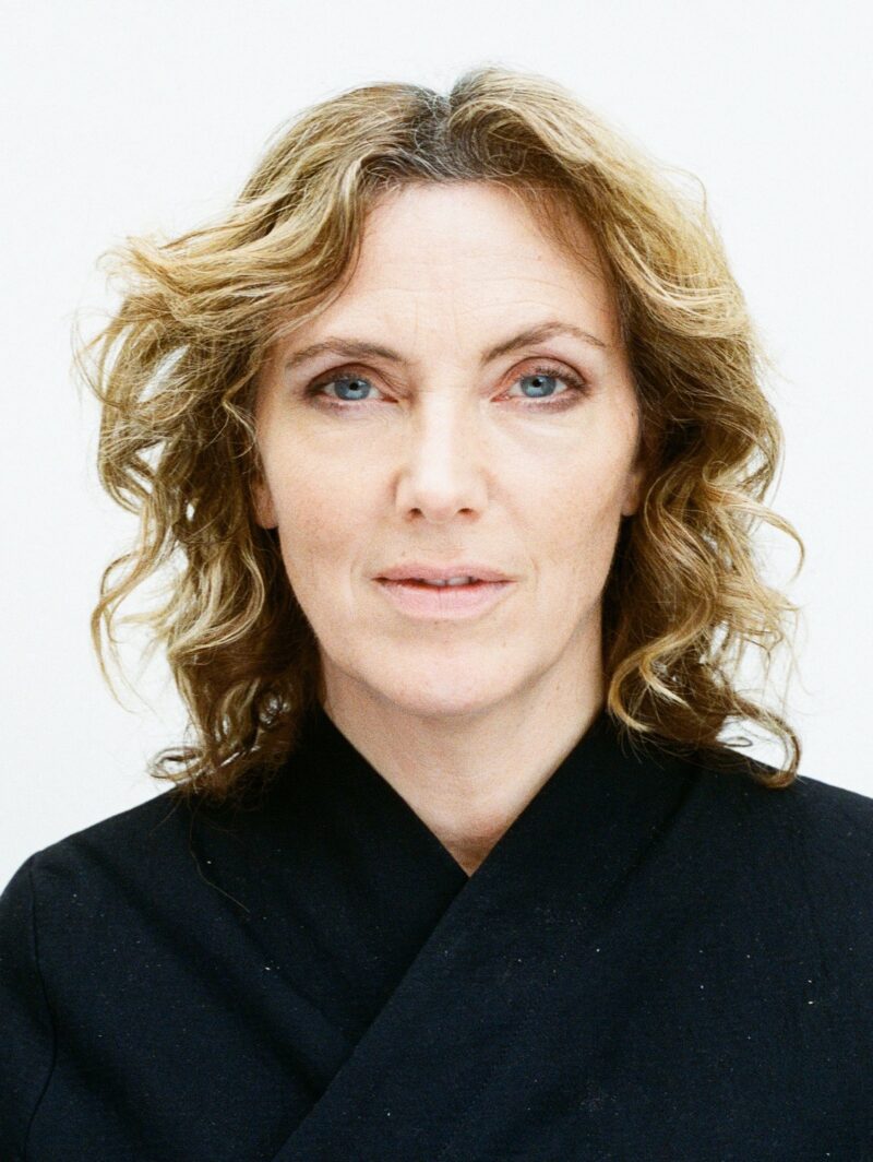 A portrait of Faye Toogood, a woman with wavy blonde hair in a black jacket.
