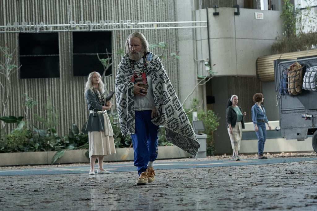 A man with grey hair wrapped in a blanket walks away from a woman with white hair inside Severn City Airport (played by the brutalist Ontario Science Centre) in a still from the television show Station Eleven.