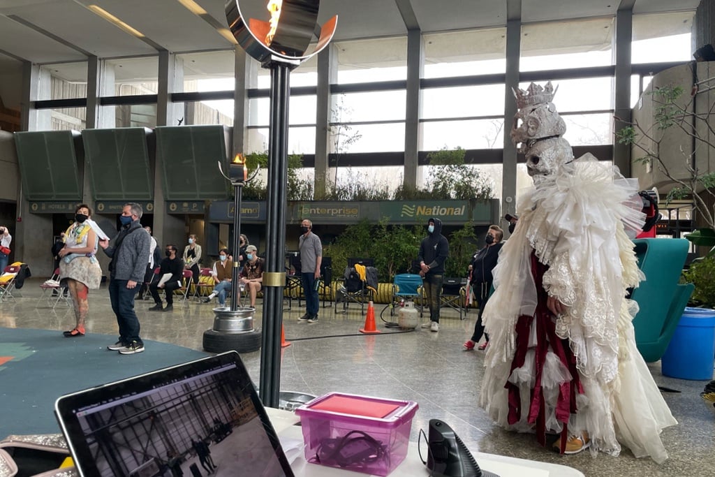 A photo of the Severn City Airport set from Station Eleven showing a character dressed as the ghost of Hamlet's father, in tulle and two stacked skull masks, inside of the brutalist Ontario Science Centre.