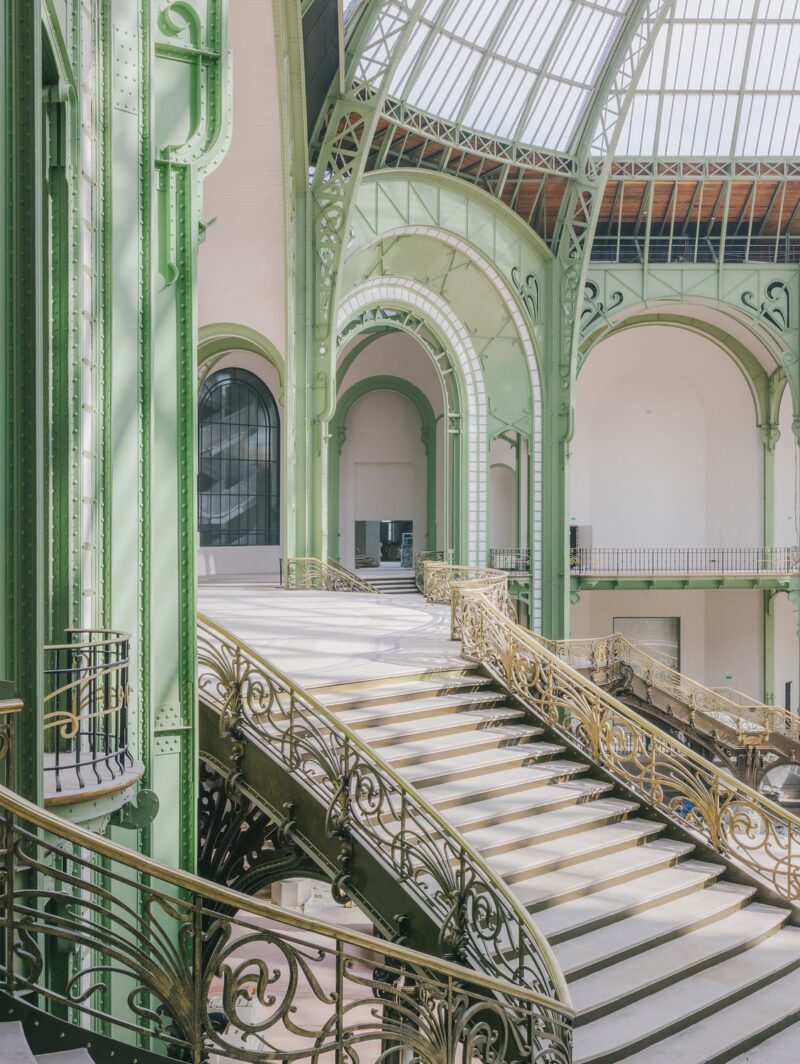 The staircase in the nave of the Paris Grand Palais, featuring elaborate metalwork railings and a glass ceiling above.