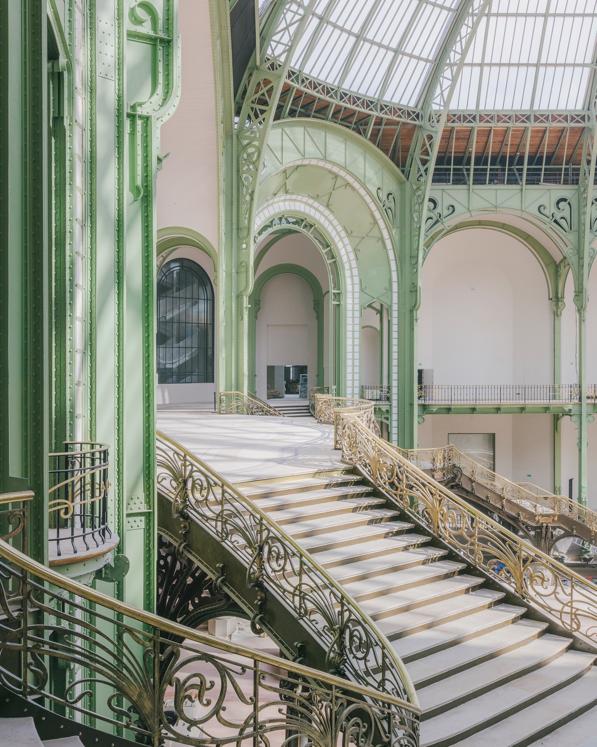 The staircase in the nave of the Paris Grand Palais, featuring elaborate metalwork railings and a glass ceiling above.