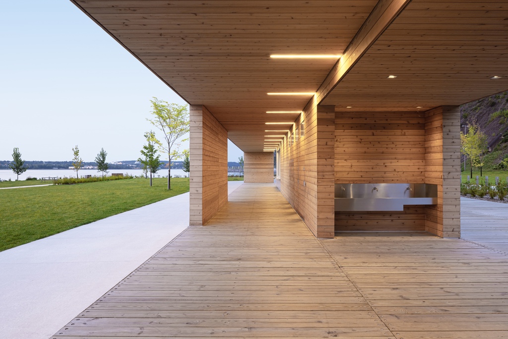 An open-air wood beach pavilion at Promenade Samuel-de Champlain in Quebec City featuring a stainless steel water fountain underneath a wood roof with lights.
