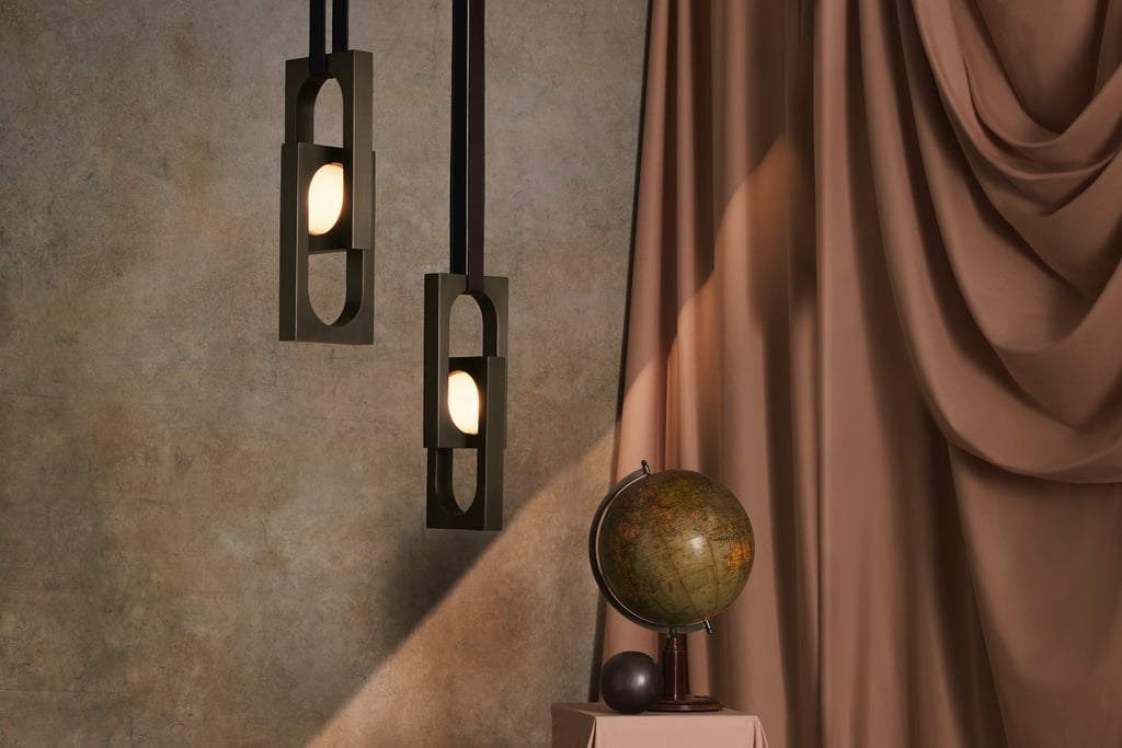 Two hanging pendants encase glowing orbs inside of rectangular brass frames hanging from leather straps.