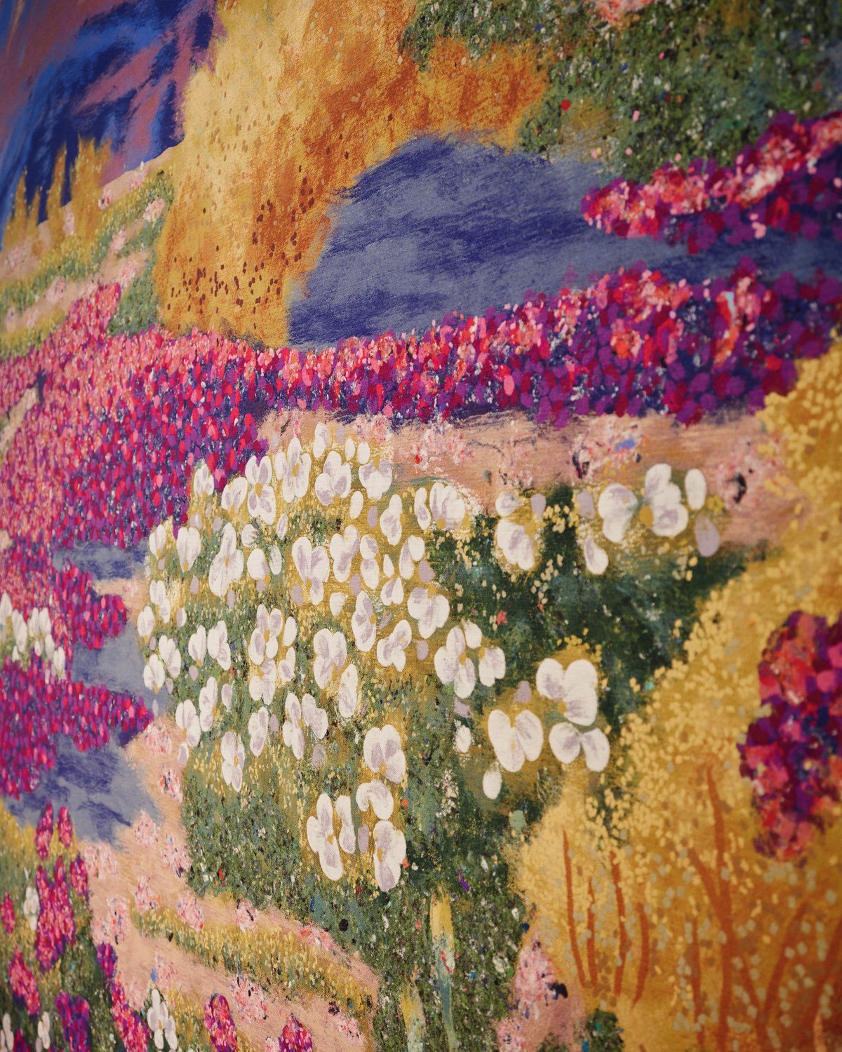 A closeup of a modern cottagecore textile wall covering design showing a rural field filled with flowers in vibrant oranges and purples.