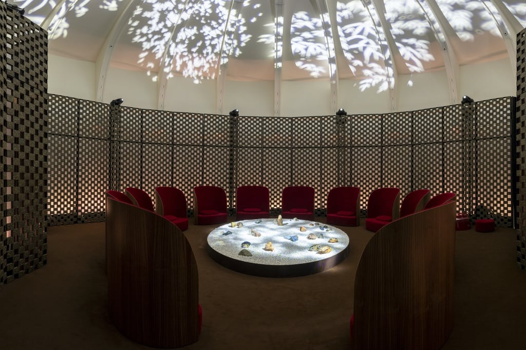 A screen wraps around a domed room with chairs surrounding a glowing table and projections on the roof. Part of an exhibition by designer Jiang Qiong Er.