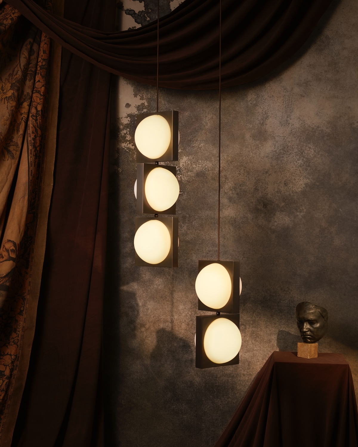 Two Solstice pendants from the Alchemist collection by Lee Broom. The one on the left has three glowing orbs mounted inside of brushed brass square frames, and the one on the right has two.