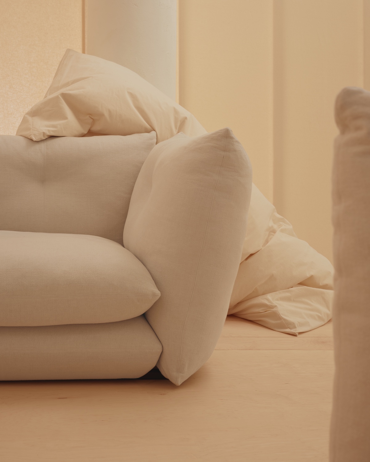 One end of the Pillo sofa by Knoll, which resembles a stack of oversized pillows. It is shown in a cream hue in a matching cream-coloured room.