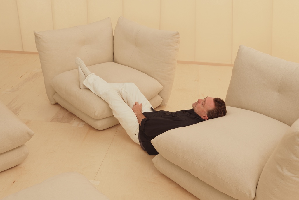 Wearing a black shirt and white pants, designer Willo Perron kicks his feat up on a single cream-coloured corner module from Knoll's Pillo sofa.