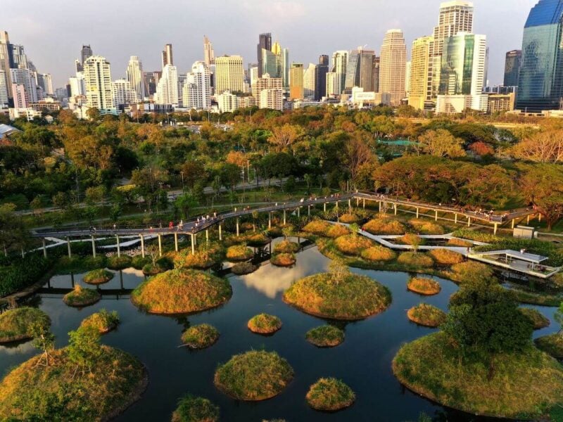 An aerial view of a partially flooded Benjakitti park, with the Bangkok skyline in the background.