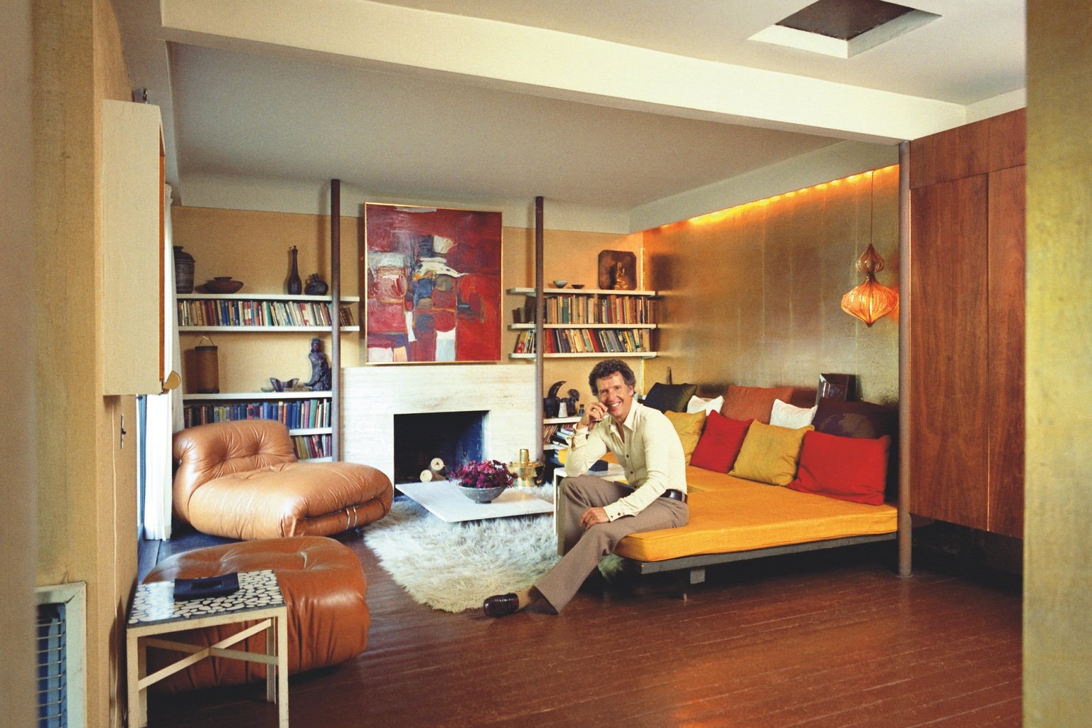 Canadian architect sitting on an orange sofa across from a buttery brown leather armchair in a wood panelled 1970s-style living room.