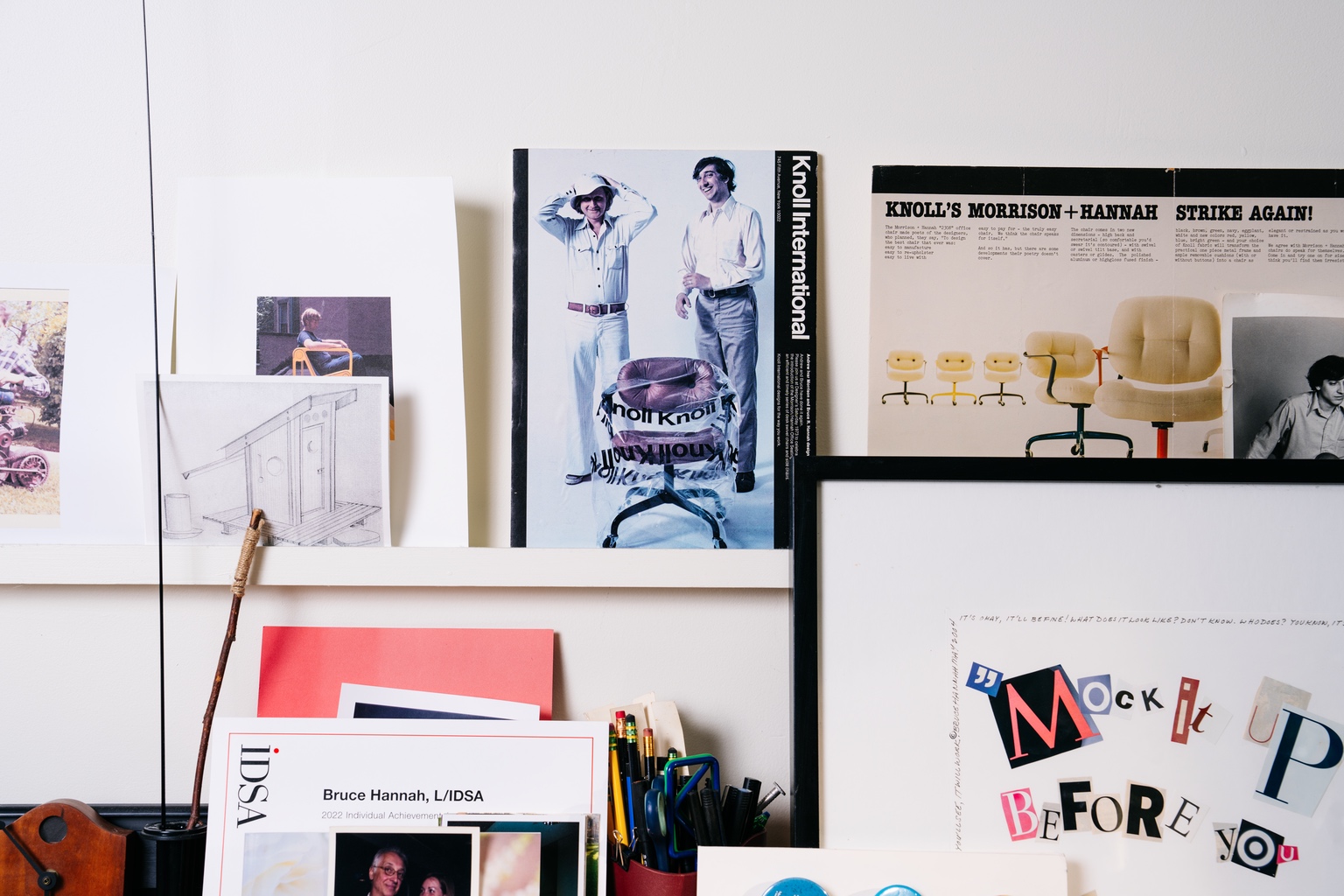 An archival photo of two designers with a friendly desk chair sits on a ledge amongst an assortment of colourful papers.