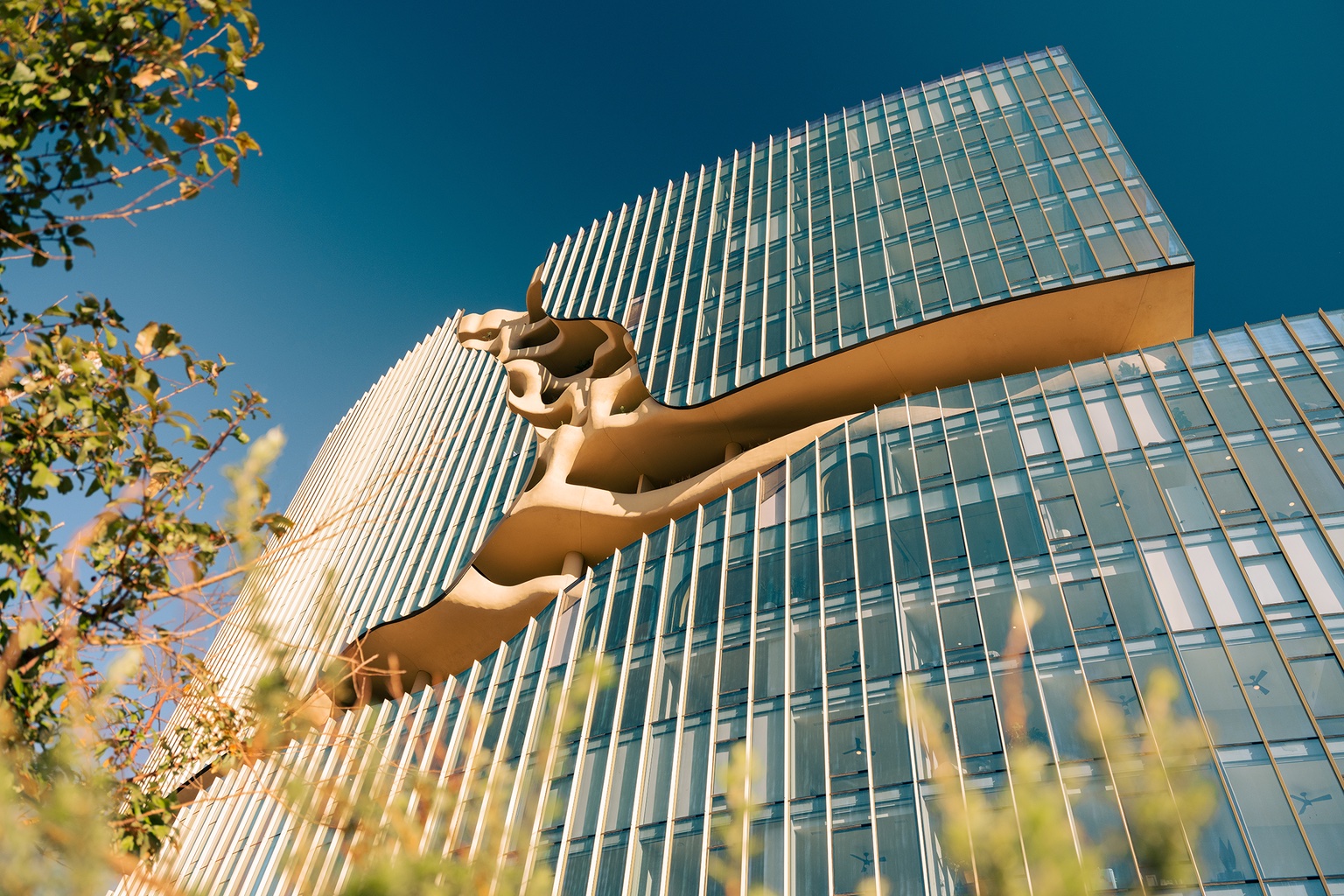 Looking up at One River North, a canyon-like residential building in Denver with exterior walkways carved into the building. The other portions of the facade are clad in glass.