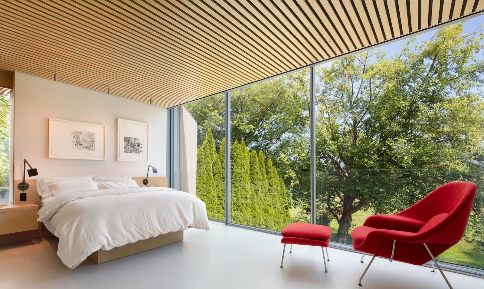 The primary bedroom is furnished with a custom-designed bed and floating side tables. Knoll’s Womb chair, in red, completes the scene.