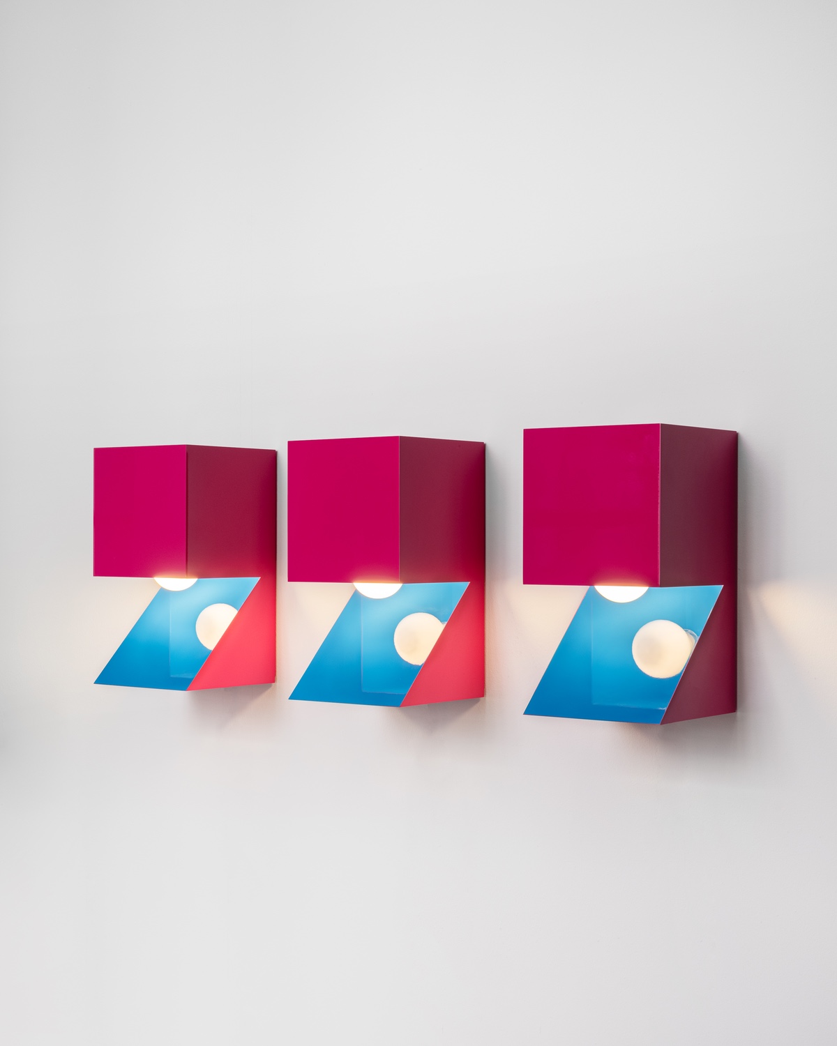 A series of three angular pink sconces.