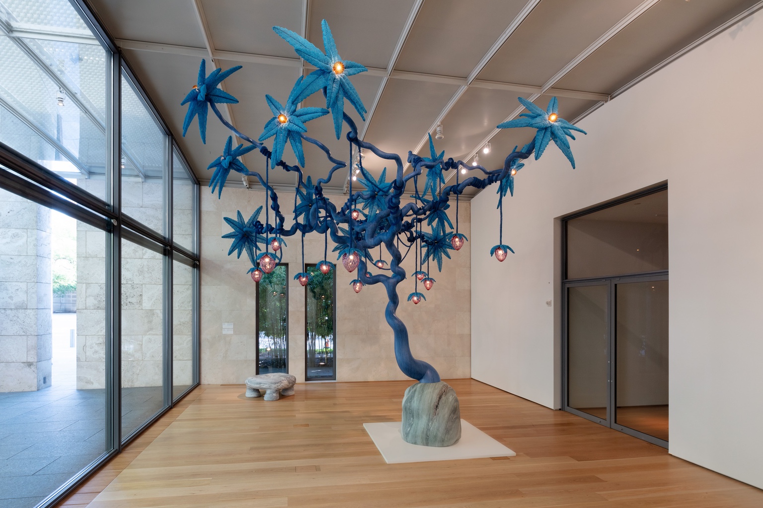 A sculpture of a blue tree with glowing pink strawberries hanging from it.