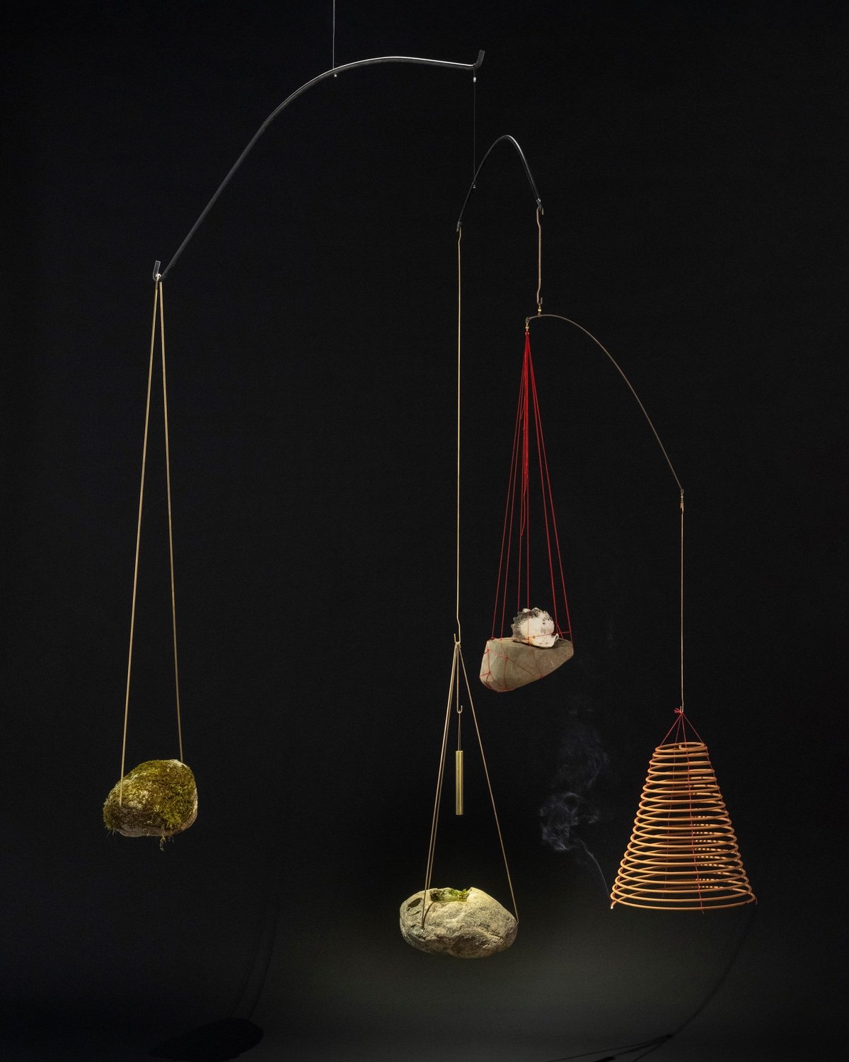 Artist Dennis Lin designs mobiles that hang remnants of his former home from steel branches. This one has four branches. Three hold rocks and charred remains and one holds spiral incense.