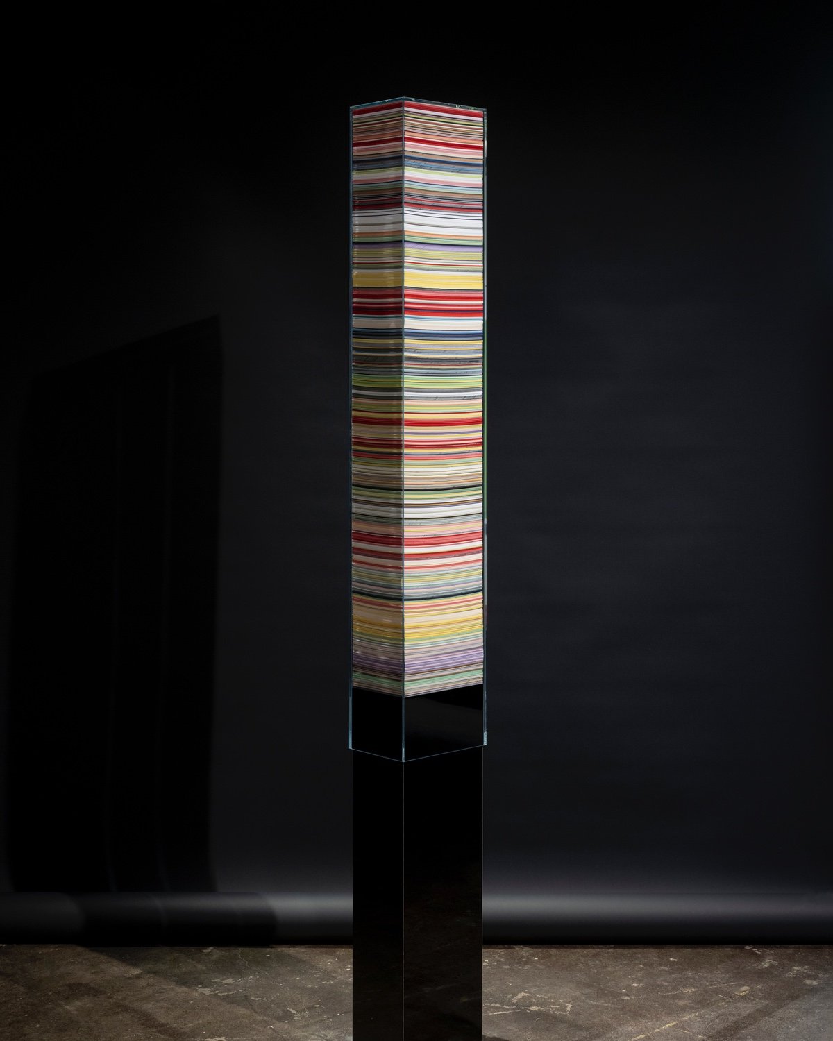 A tall stack of multicoloured paper is encased inside of a plastic frame.