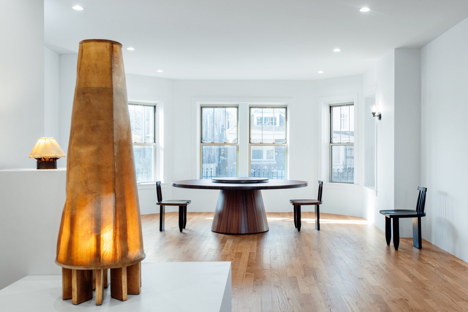 A view of a gallery showing furniture by football player turned designer Michael Bennett. The designs shown include a floor lamp to the left and a round dining table surrounded by chairs at the back of the room.