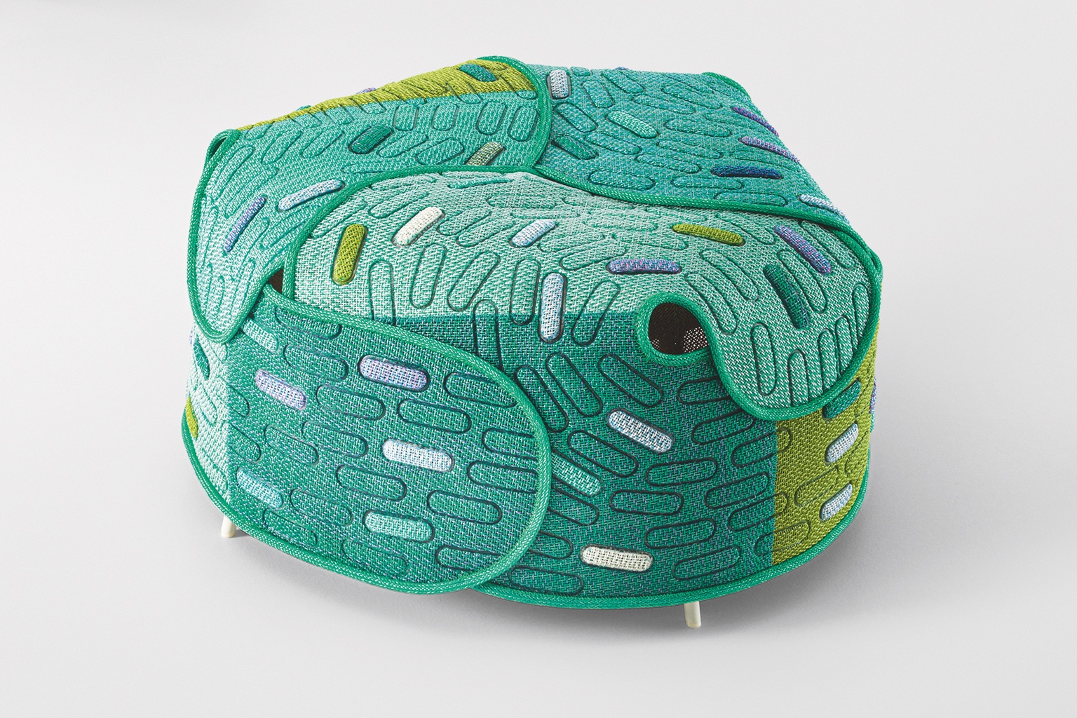 A green ottoman made from curved sheets of material with pill-shaped pods in different colours on it.
