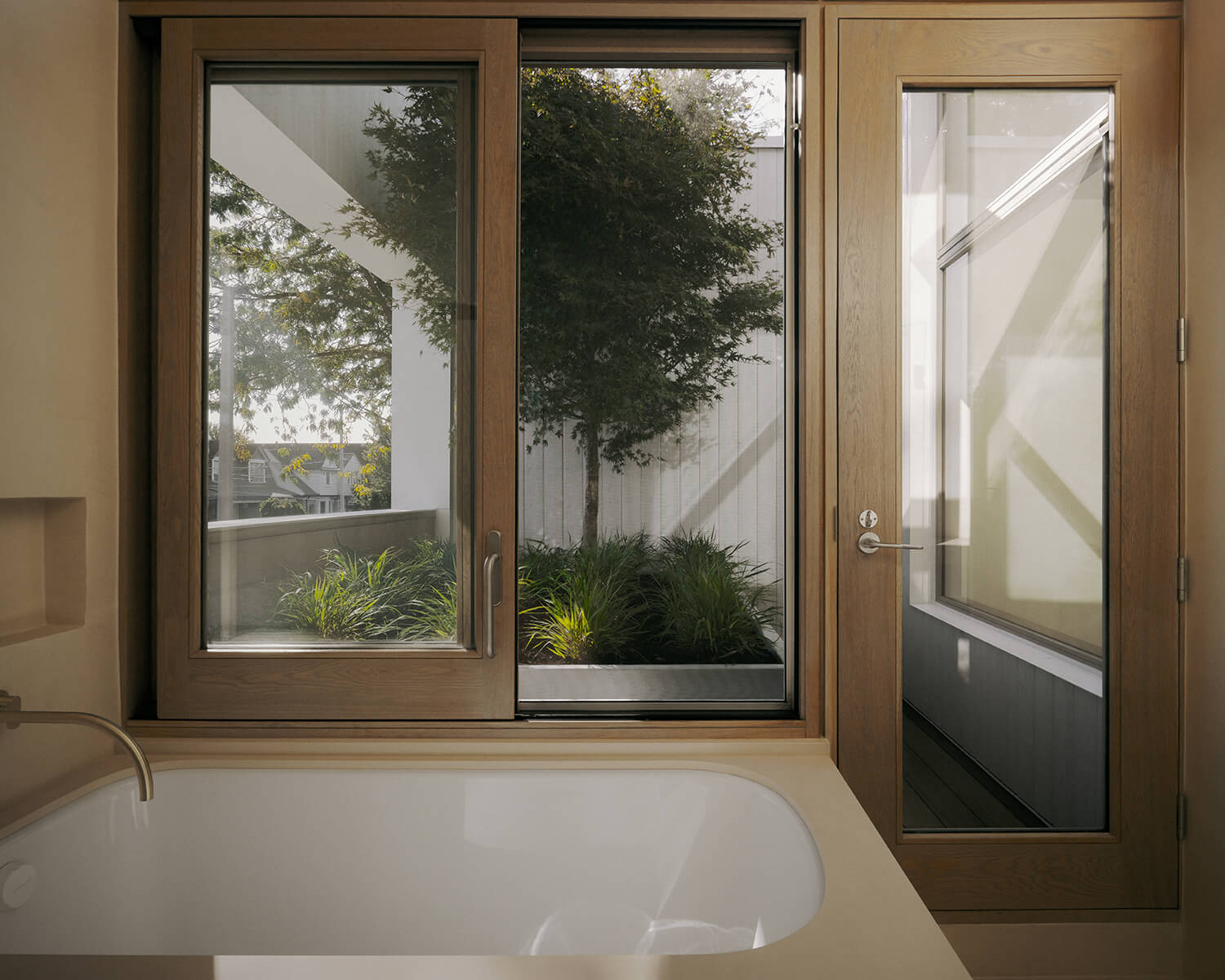 By swinging open a window, the family in the north unit can enjoy a bath en plein air — and a view to the breeze-filtering maple. The doors and windows throughout the home were manufactured by Bauhaus.
