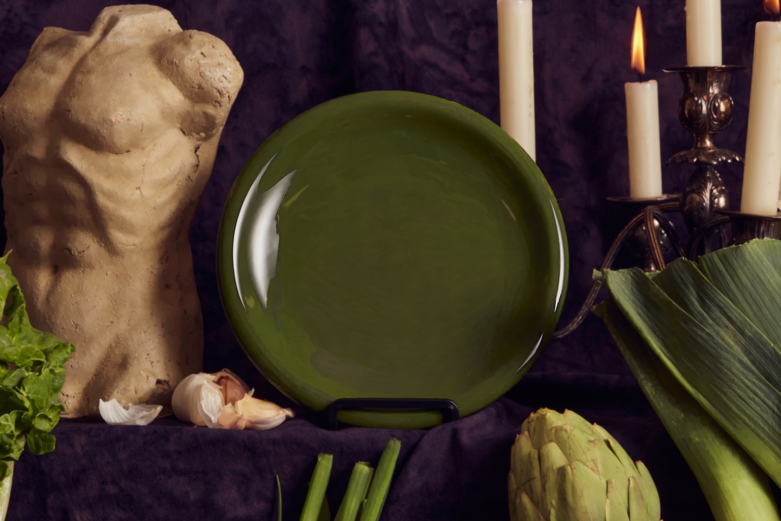 A small green plate. It's shown as part of a still life, with a small torso bust on one side and a candelabra on the other.