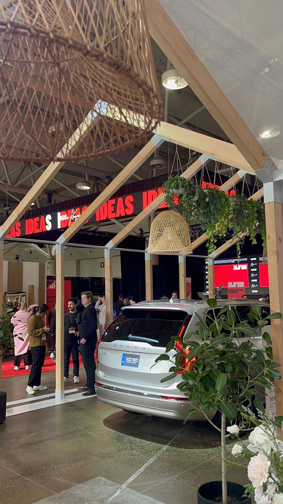 A silver Volvo XC90 parked under a simple timber frame with hanging plants at IDS 2025.