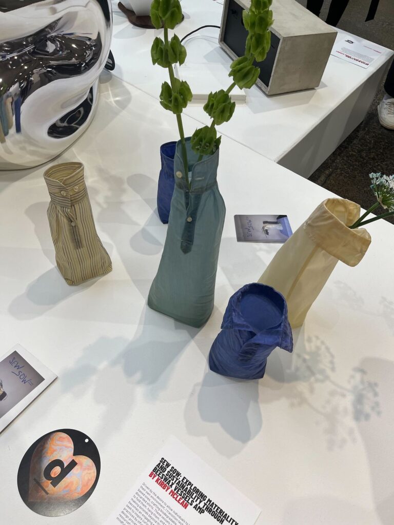 Elongated turquoise, blue and beige beeswax vessels containing flowers, by Kirby Mclean, at IDS 2025.