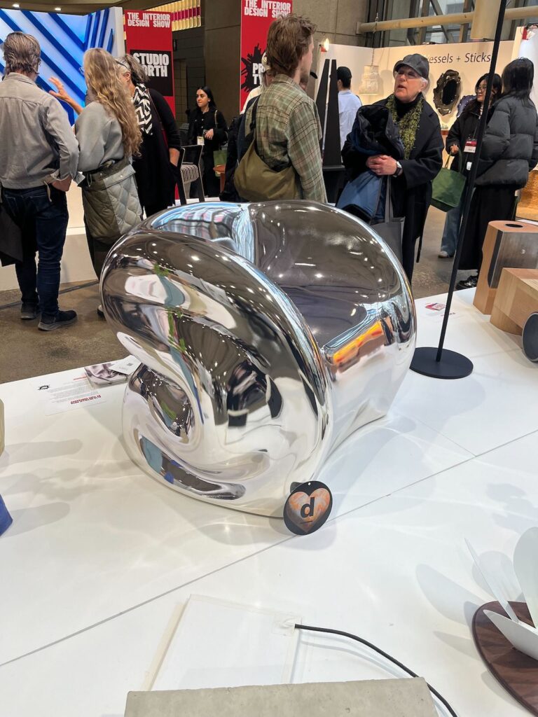 A curving, reflective silver fibreglass-coated chair by Yury Goncharov at IDS 2025's Prototype Showcase.