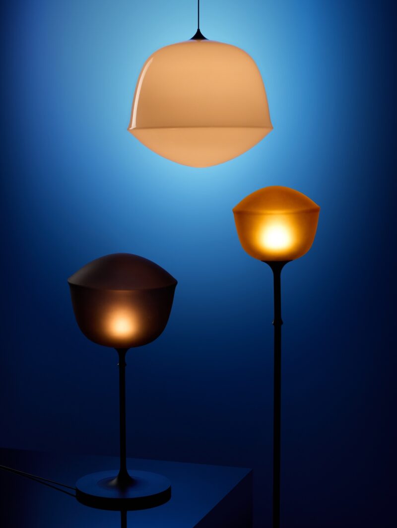 A trio of lamps — a table lamp, floor lamp and pendant — with bell-shaped shades. Each one has a different finish — one is dark and frosted, one is opaque, and the other has a golden frosted treatment.