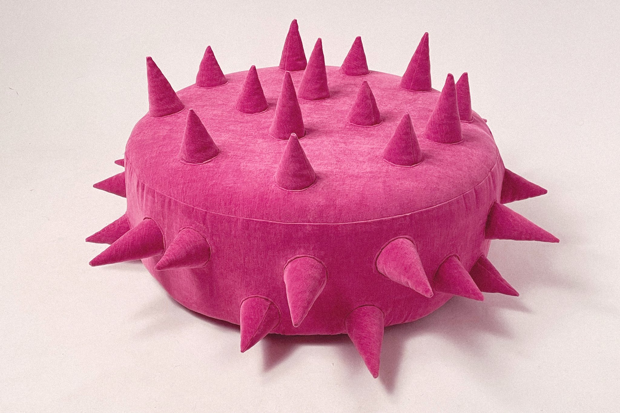 An upholstered pink circular lounge chair with protruding upholstered spikes.