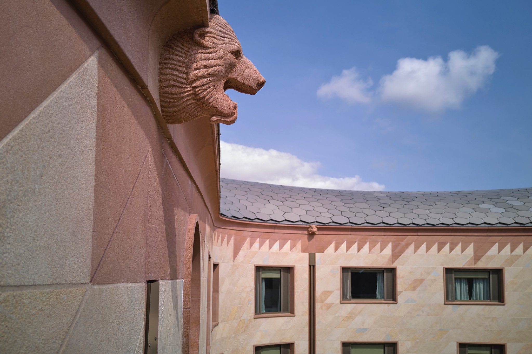 A gargoyle below the roofline of the Gradel Quadrangles, which features zig-zag geometric tiling below the roof clad in fish scale-like tiles.